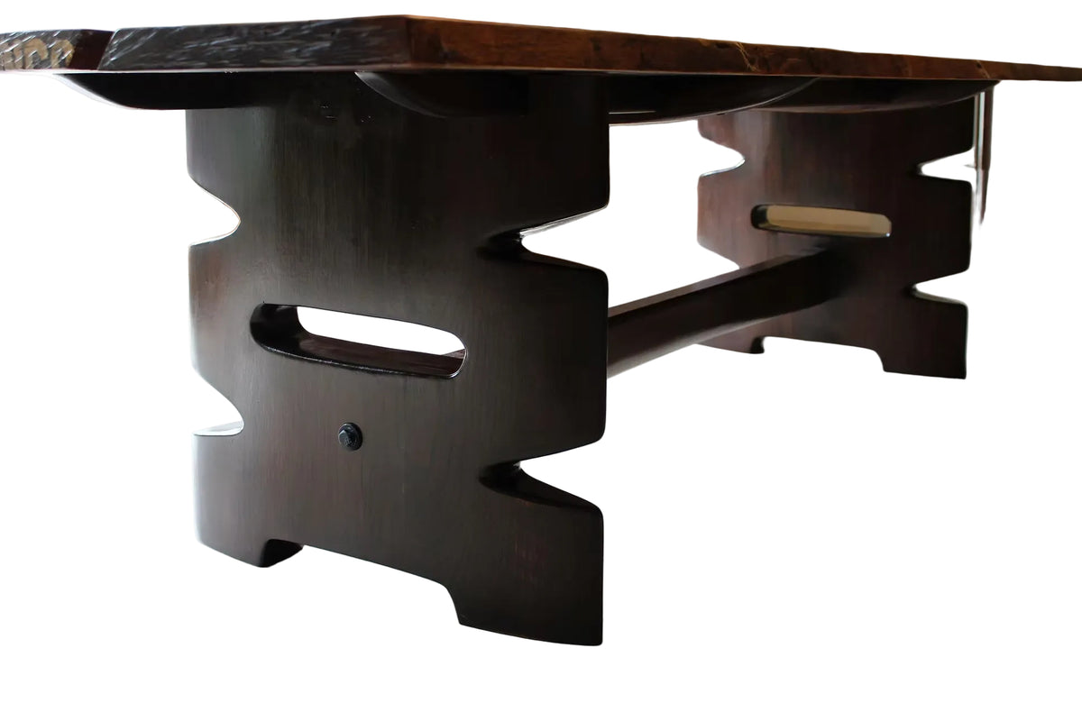 A dark wood boardroom table with a thick live-edge top and sculptural, asymmetrical legs with cutout details